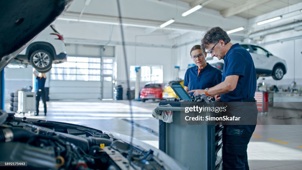 Manager And Mechanic Evaluating The Car Engine Using Laptop At Workshop