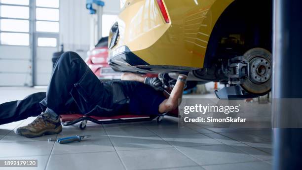 male mechanic on creeper working under car at workshop - onder stockfoto's en -beelden