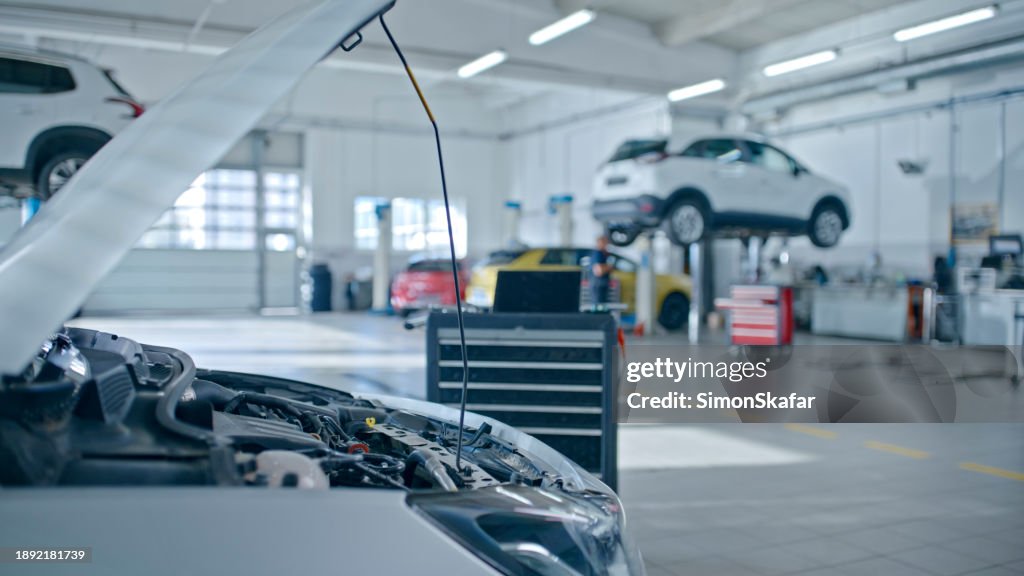 Autos öffnen die Motorhaube mit Laptop, der neben dem Motor in der Autowerkstatt platziert ist