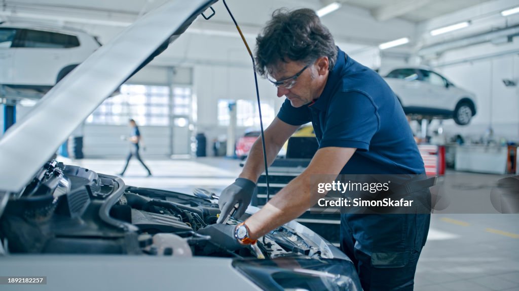 Mecânico masculino trabalhando no motor do carro na oficina de reparação de automóveis