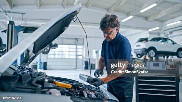 männlicher mechaniker, der am automotor in der autowerkstatt arbeitet - maschinenteil hergestellter gegenstand stock-fotos und bilder