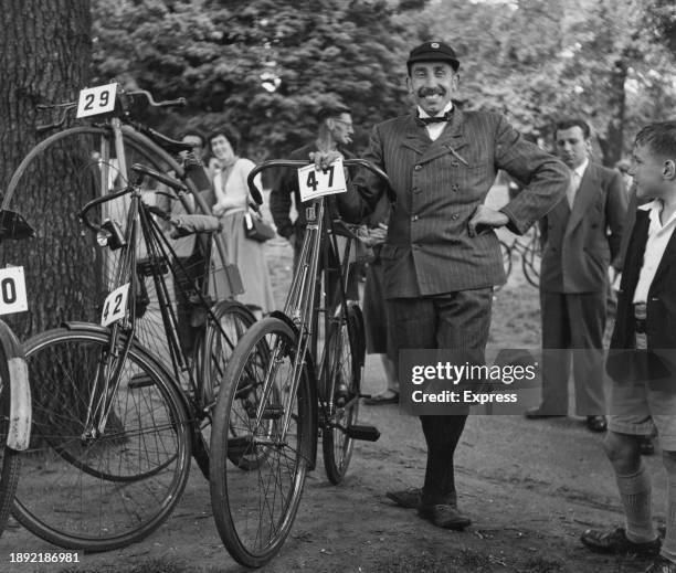 Man posing next to a Dursley Pedersen bike during a cycling event, circa 1900. He is wearing a four-button suit, knee breeches, a bow tie and club...