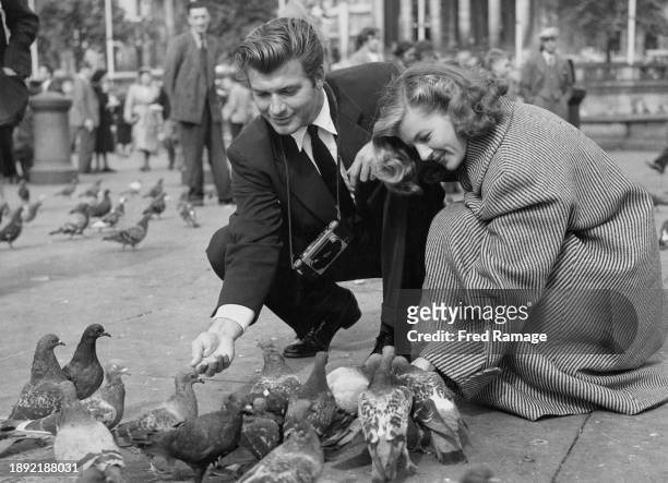 French actress Corinne Calvet and her husband, American actor John Bromfield , feeding pigeons in Trafalgar Square during a visit to London,...