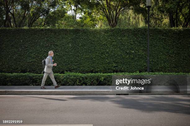 senior businessman walking with a backpack - pavement stock pictures, royalty-free photos & images
