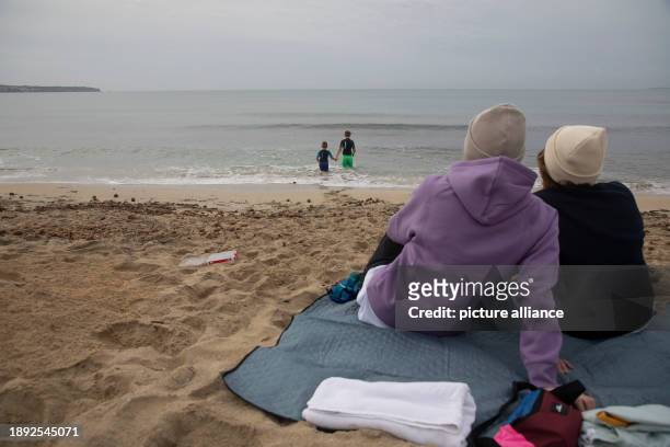 January 2024, Spain, Palma: Sabine and Sonja from Cologne sit on the beach promenade of Arenal in cloudy weather on New Year's Day while two boys...