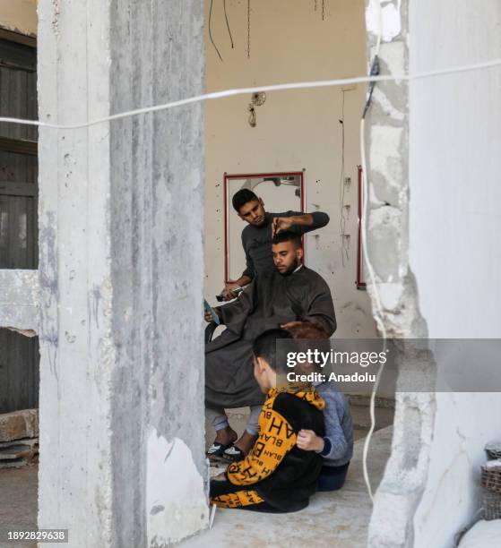 Palestinian barber cuts a client's hair to make a living among the rubble of a barber shop damaged after Israeli attacks as people try to continue...