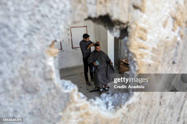 Palestinian barber cuts a client's hair to make a living among the rubble of a barber shop damaged after Israeli attacks as people try to continue...