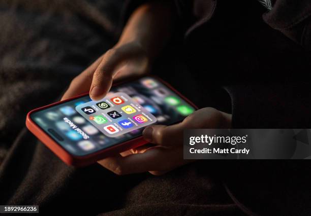 Year-old boy looks at an iPhone screen showing various social media apps including TikTok, Facebook and X, on December 19, 2023 in Bath, England. The...