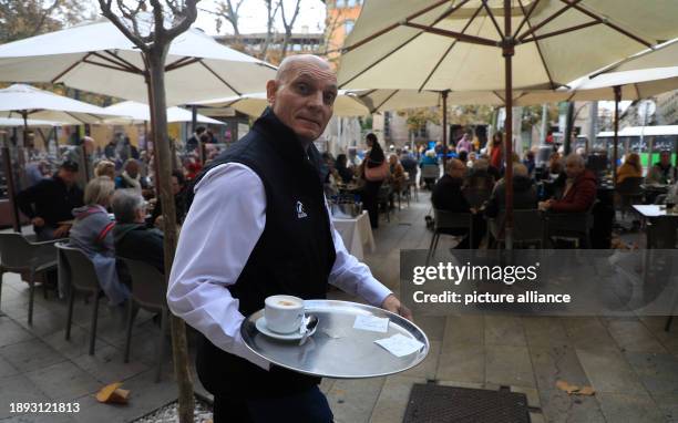 December 2023, Spain, Palma: Miguel, waiter, serves a coffee on the last day of the year on a crowded terrace of a bar in Palma. For many Europeans,...