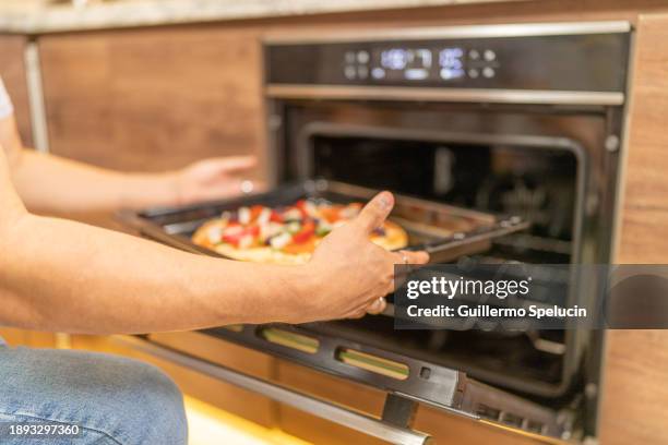 man putting freshly prepared pizza in the oven - pizza temptation stock pictures, royalty-free photos & images