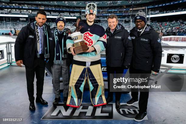 Paul Bissonnette, Liam McHugh, Wayne Gretzky, and Anson Carter pose with Joey Daccord of the Seattle Kraken as Daccord holds the MVP Cocoa Cup after...