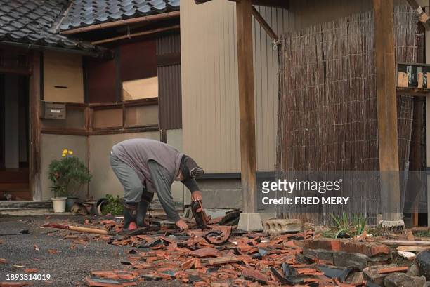 This screen grab from AFPTV video footage taken on January 2, 2024 shows a man clearing debris in front of a house in the Japanese city of Nanao,...
