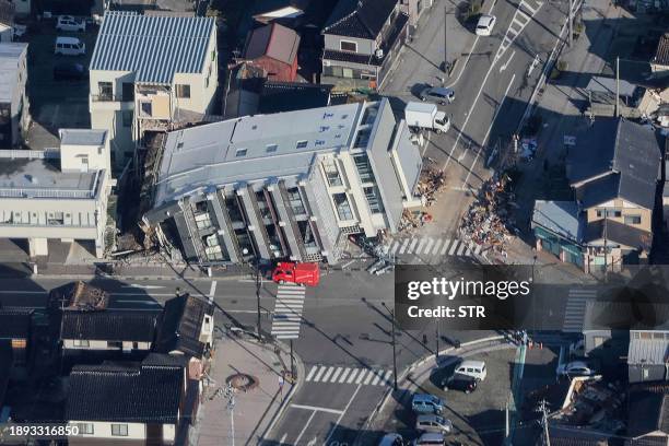 This aerial photo provided by Jiji Press shows a rescue vehicle parked next to a seven-storey building which fell over in Wajima, Ishikawa prefecture...