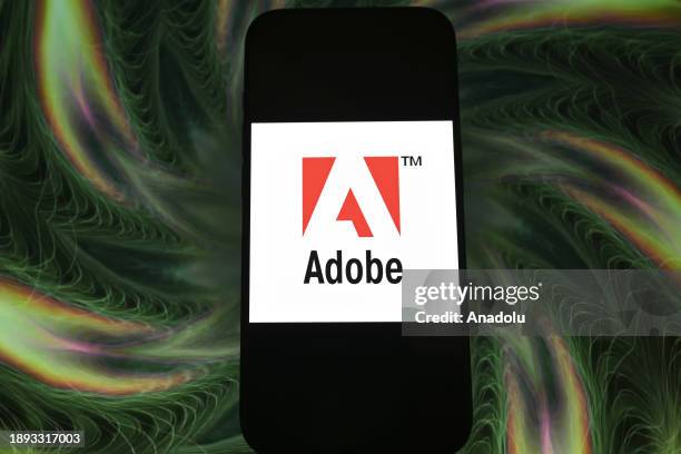 In this photo illustration logo of 'Adobe' app is displayed on a mobile screen in front of a computer screen in Ankara, Turkiye on December 28, 2023.