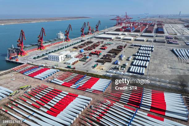 The photo taken on January 1, 2024 shows wind turbine blades and cargo containers stacked at a port in Nantong, in China's eastern Jiangsu province....