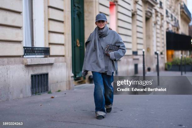 Diane Batoukina wears a gray cap, a gray wool large scarf, and matching double breasted coat by World of Stylein, blue sneakers shoes, blue wide-leg...