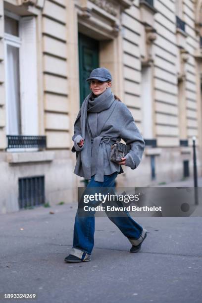 Diane Batoukina wears a gray cap, a gray wool large scarf, and matching double breasted coat by World of Stylein, blue sneakers shoes, blue wide-leg...