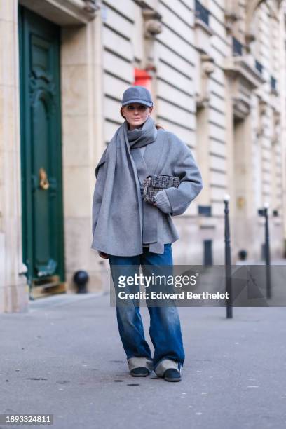 Diane Batoukina wears a gray cap, a gray wool large scarf, and matching double breasted coat by World of Stylein, blue sneakers shoes, blue wide-leg...