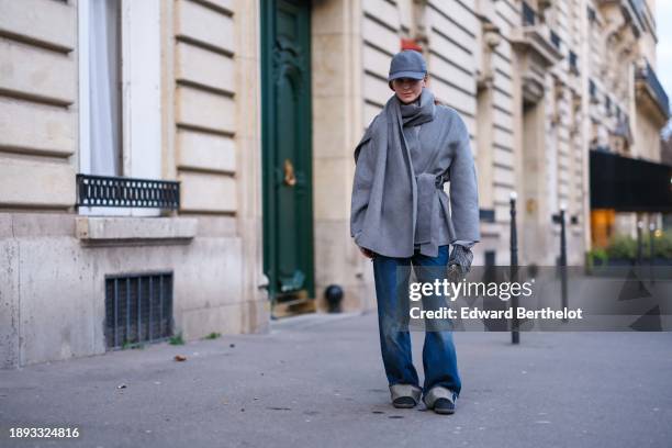 Diane Batoukina wears a gray cap, a gray wool large scarf, and matching double breasted coat by World of Stylein, blue sneakers shoes, blue wide-leg...