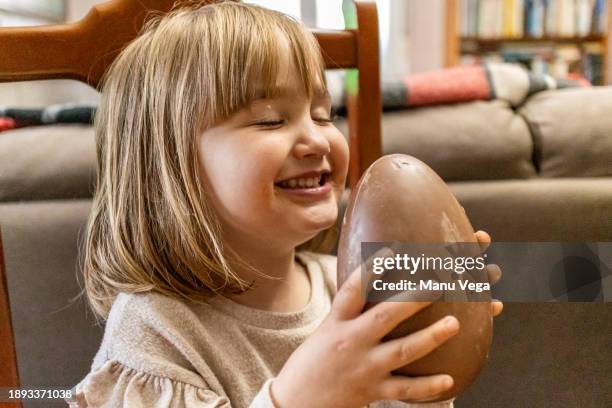 a happy little girl with her eyes closed holding a chocolate easter egg at home - milk chocolate stock pictures, royalty-free photos & images