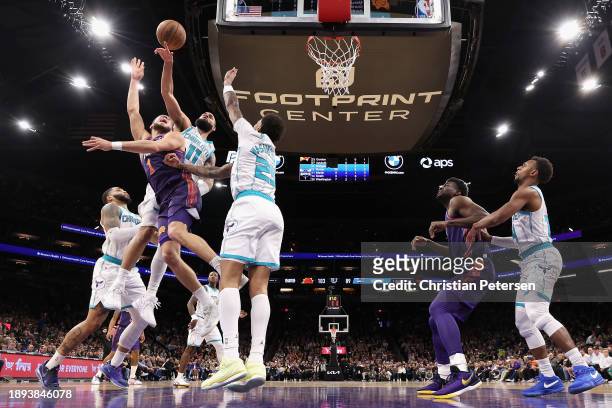 Devin Booker of the Phoenix Suns attempts a shot over Cody Martin and P.J. Washington of the Charlotte Hornets during the second half of the NBA game...