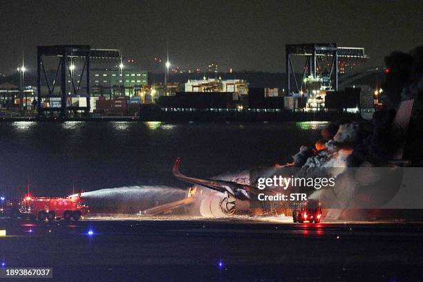 This photo provided by Jiji Press shows firefighters attempting to extinguish a fire on a Japan Airlines plane on a runway of Tokyo's Haneda Airport...
