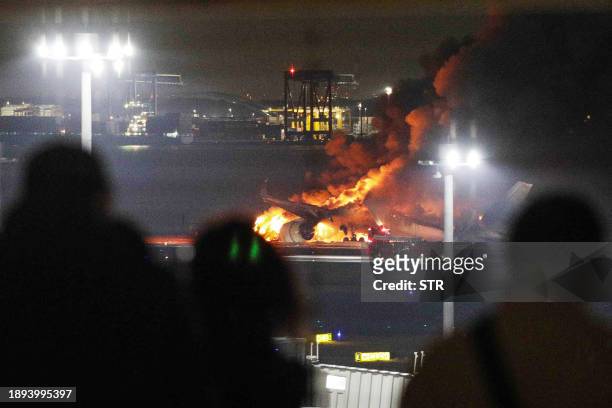 This photo provided by Jiji Press shows people on an observation deck looking at a Japan Airlines plane on fire on a runway of Tokyo's Haneda Airport...