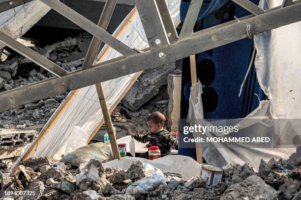 Child holds a plate while sitting between rubble in Rafah in the southern Gaza Strip on January 2 amid the ongoing conflict between Israel and the...