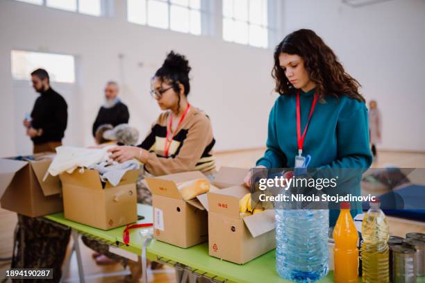 volunteers sorting, packing clothes in cardboard boxes - banco alimentar imagens e fotografias de stock