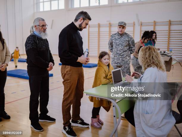 freiwilliger unterhält sich mit einem flüchtling, während er den laptop in einer flüchtlingsunterkunft benutzt - flüchtlingsunterkunft stock-fotos und bilder