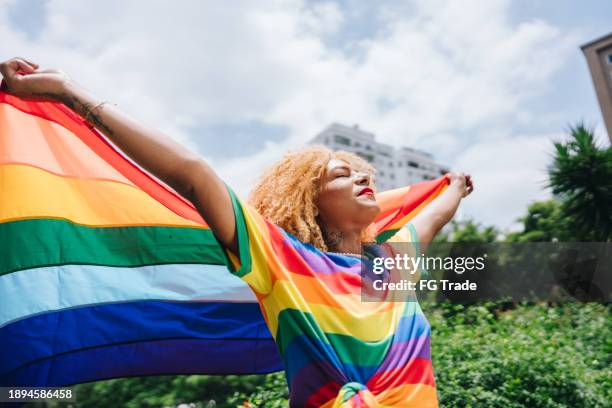 une femme transgenre tenant un drapeau arc-en-ciel à l’extérieur - mois des fiertés lgbtqia photos et images de collection