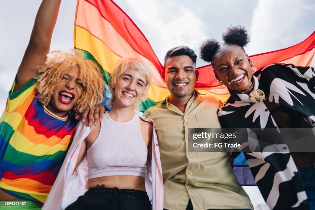 Portrait of a lgbtqia+ friends holding a rainbow flag outdoors