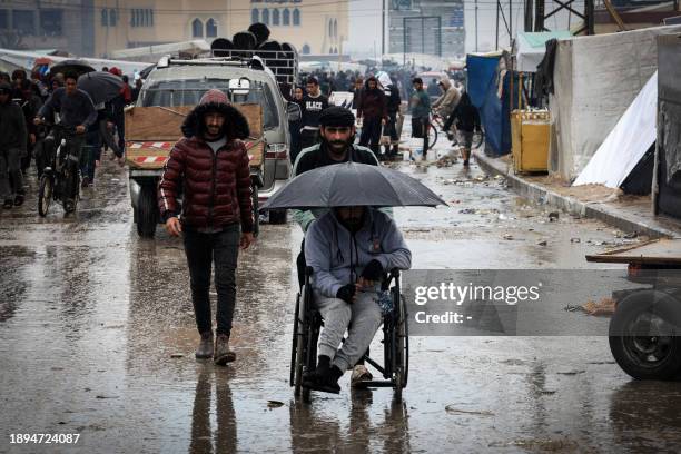 Palestinian man on a wheelchair is pushed on a street under the rain at a makeshift camp housing displaced Palestinians, in Rafah in the southern...
