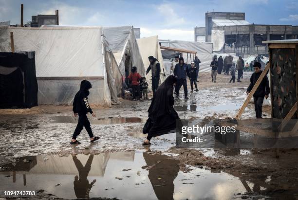 Palestinians make their way on a muddy path past tents at a makeshift camp housing displaced Palestinians, in Rafah in the southern Gaza Strip, amid...