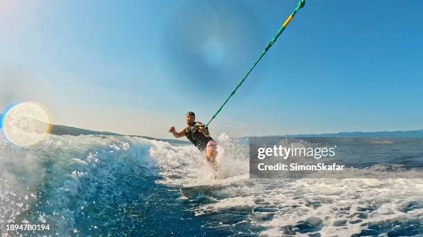 mann hält seil und genießt wakeboarden im meer an einem sonnigen tag mit blauem himmel - wasserski stock-fotos und bilder