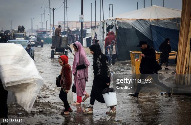 Palestinians cross a flooded street at a makeshift camp housing displaced Palestinians, in Rafah in the southern Gaza Strip, amid the ongoing...