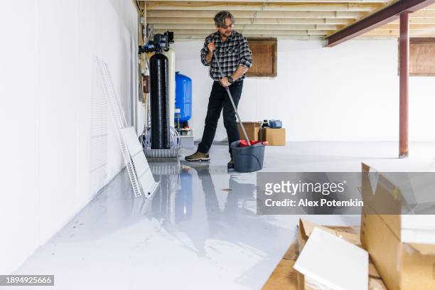 clean up after basement flooding: mature homeowner with a mop drains water into the sewer - flood cleanup stock pictures, royalty-free photos & images