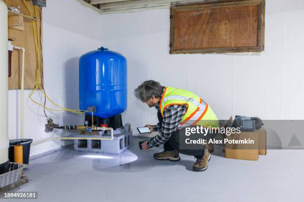 réservoir d’eau sous pression brisé dans un sous-sol inondé. un inspecteur mature photographie des dommages à un tuyau dans une cave inondée - pompe à eau photos et images de collection
