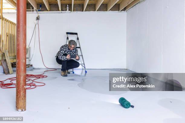 basement flooding: mature homeowner photographing flooded floor to prove the extent of the damage. - flooded basement stock pictures, royalty-free photos & images