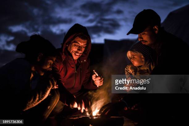 Palestinian families warm themselves near a fire during cold weather as they try to continue their daily lives under harsh conditions in Rafah, Gaza...