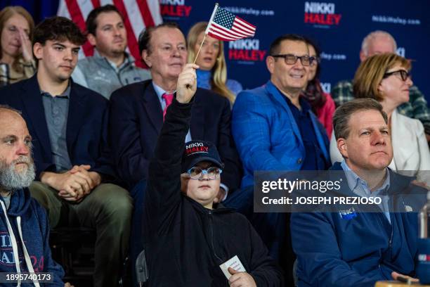 Young supporter sits next to Governor of New Hampshire Chris Sununu and waves a flag during a Nikki Haley campaign town hall event at Wentworth by...