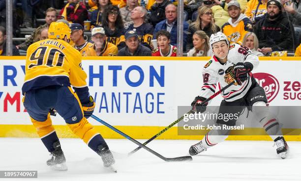 Connor Bedard of the Chicago Blackhawks passes the puck against Ryan O'Reilly of the Nashville Predators during an NHL game at Bridgestone Arena on...