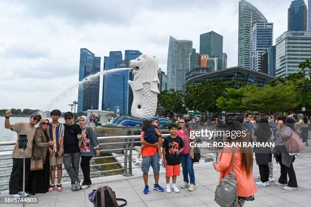 People take photographs with a backdrop of the Merlion statue along the Marina Bay waterfront in Singapore on January 3, 2024.