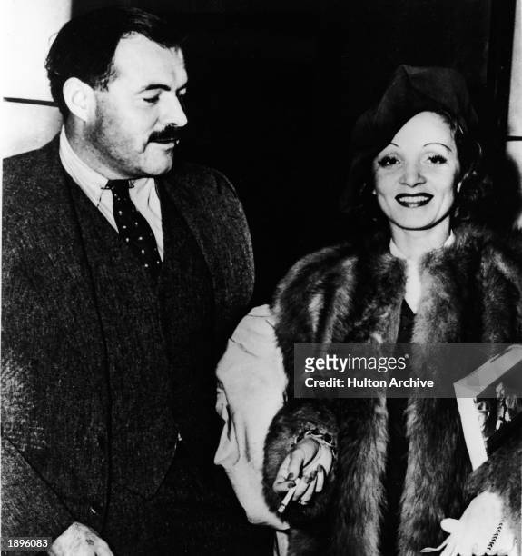 American author Ernest Hemingway and German-born actor Marlene Dietrich stand together while attending an event, 1930s. Dietrich holds a copy of one...