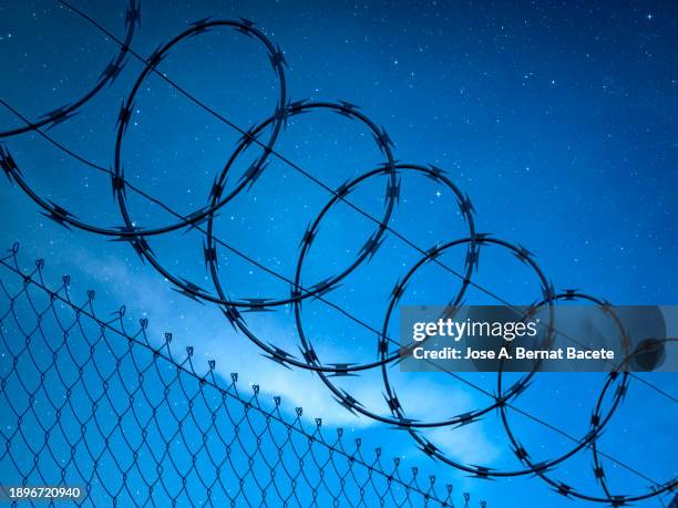 metal fence with barbed wire over a night sky full of stars. - razor wire stock pictures, royalty-free photos & images