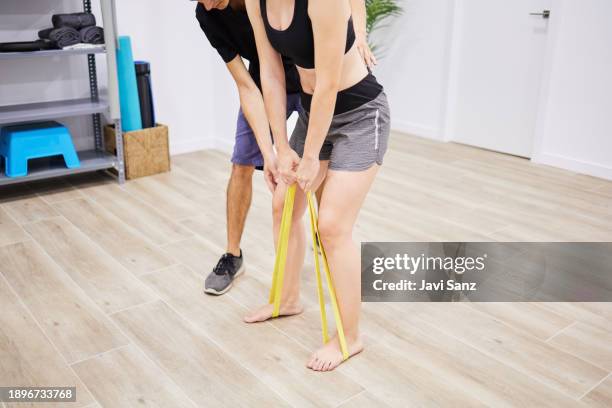 fisioterapeuta enseñando a una mujer a hacer ejercicio con una banda elástica en un hospital de rehabilitación. - goma elástica fotografías e imágenes de stock