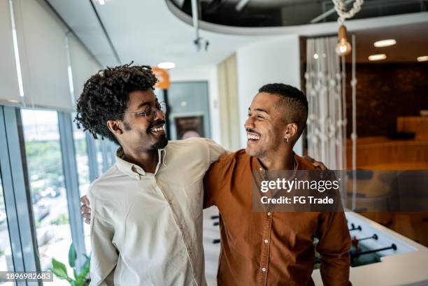 glückliche mitarbeiter umarmen sich im spielzimmer des büros - arm umlegen stock-fotos und bilder