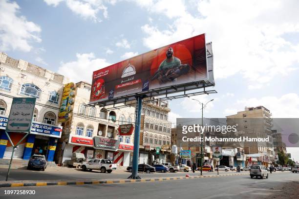 Yemenis drive under a large billboard with a picture depicting a Palestinian man carrying an injured child who is a victim of Israeli raids, and...