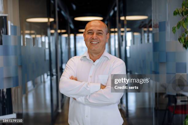 portrait of a smiling businessman standing in corridor of modern office - bald business man stock pictures, royalty-free photos & images