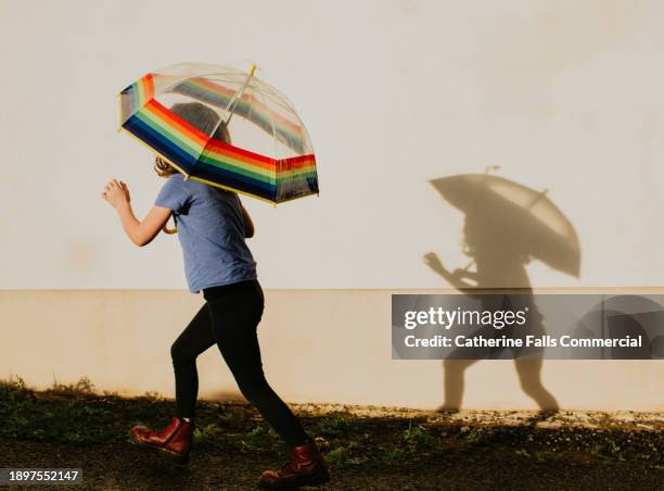 a child holds a rainbow umbrella and casts a shadow on the wall beside her - handle stock pictures, royalty-free photos & images